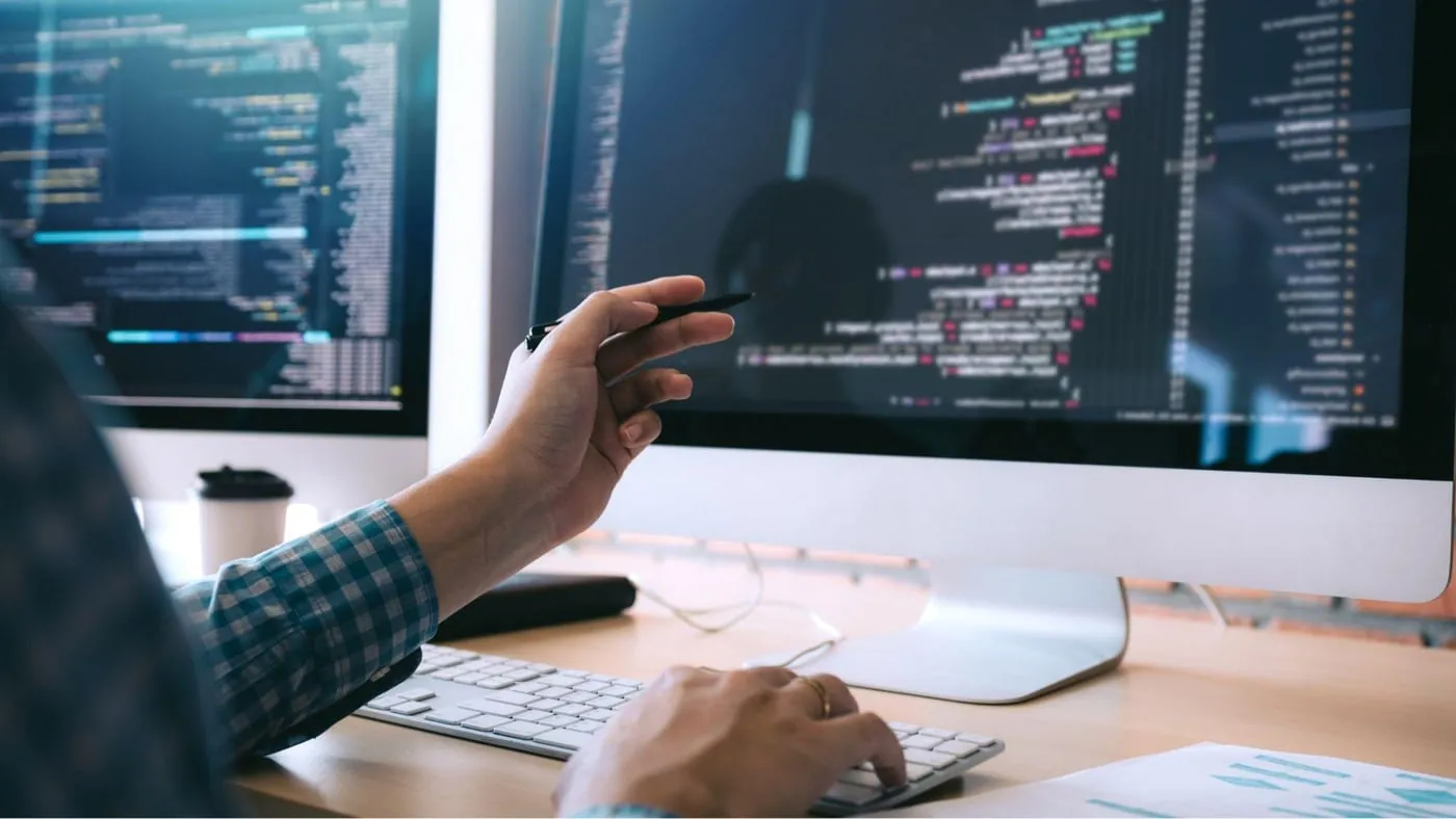 A developer reviewing pipeline code on two monitors